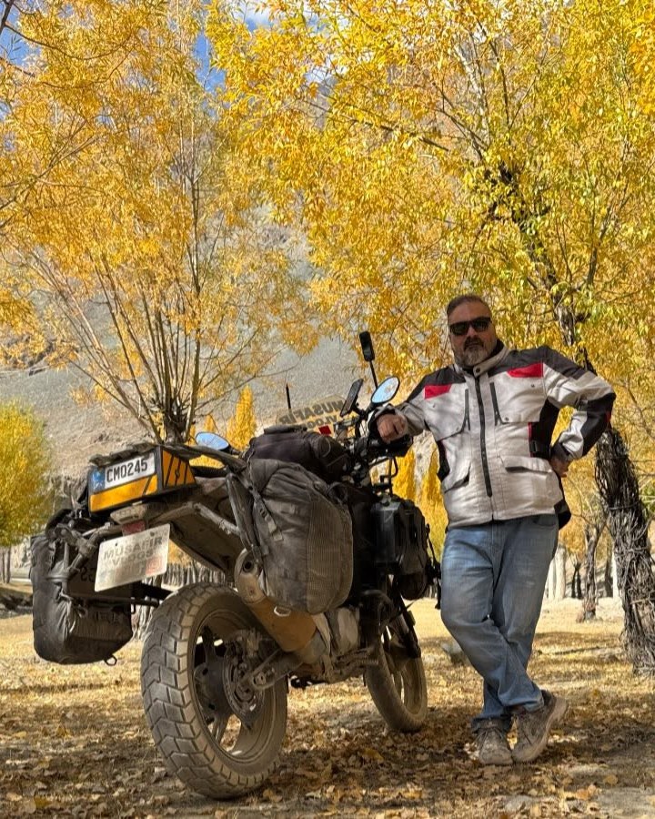 Syed Muzaffar Tirmizi with his motorcycle among autumn trees in northern Pakistan